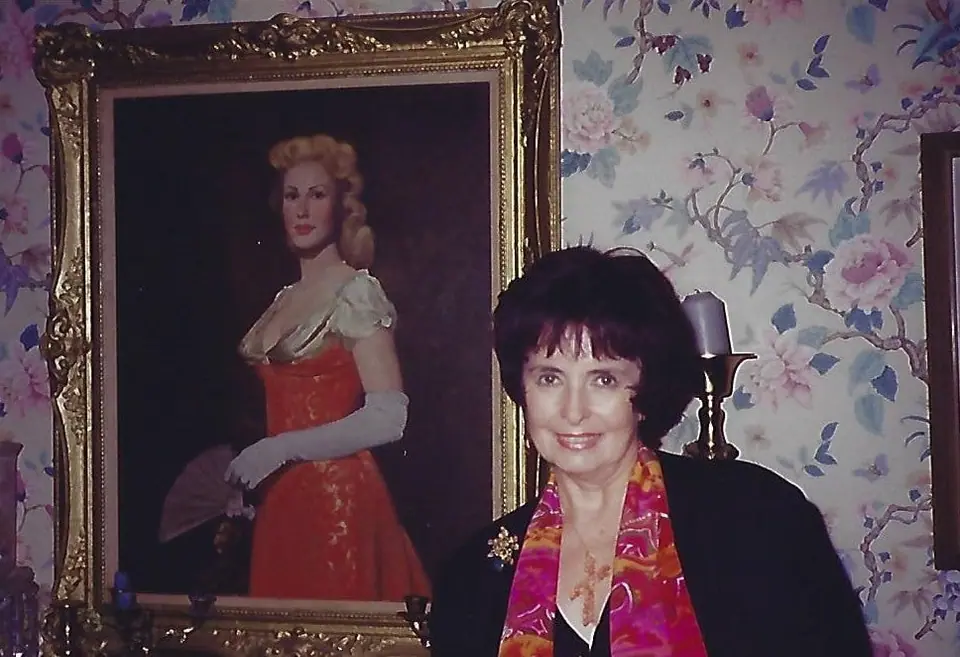 Margaret O'Brien wearing a Swoboda brooch, standing beside a gilt-framed portrait painting