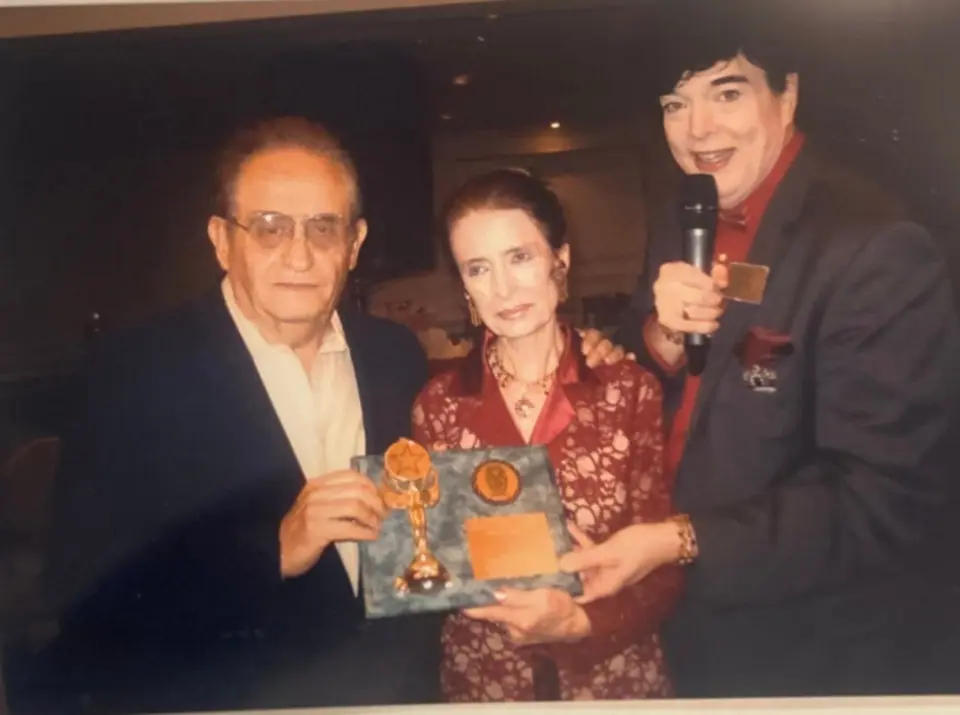 Nate Waxman and Margaret O'Brien holding an award plaque beside Randell Malone with a microphone