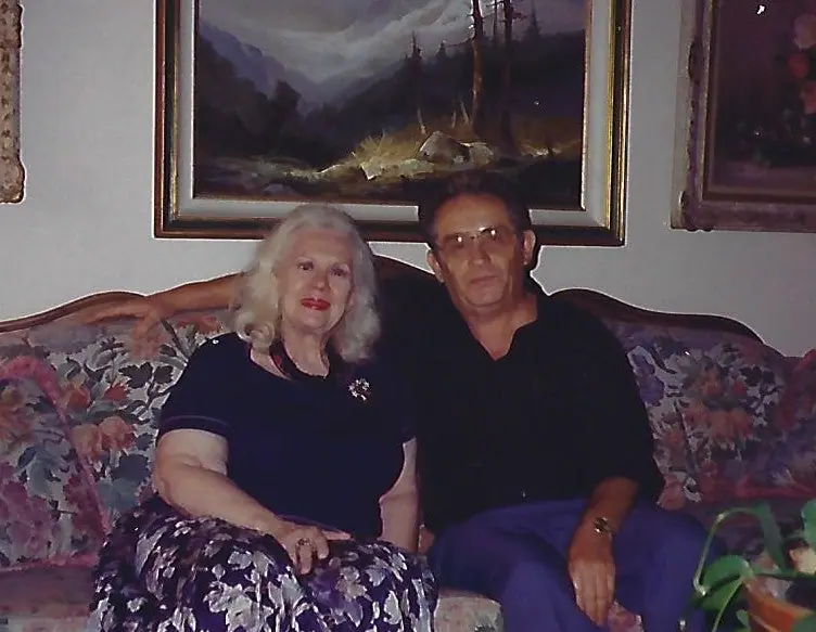 Nate Waxman and Virginia Mayo seated on a floral sofa; she wears a Swoboda brooch